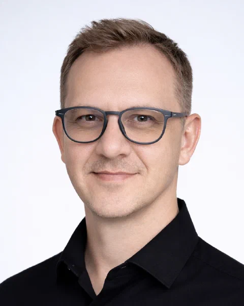 David Griesel, head and shoulders, with glasses and a dark collared shirt, looking at the camera with a slight smile.